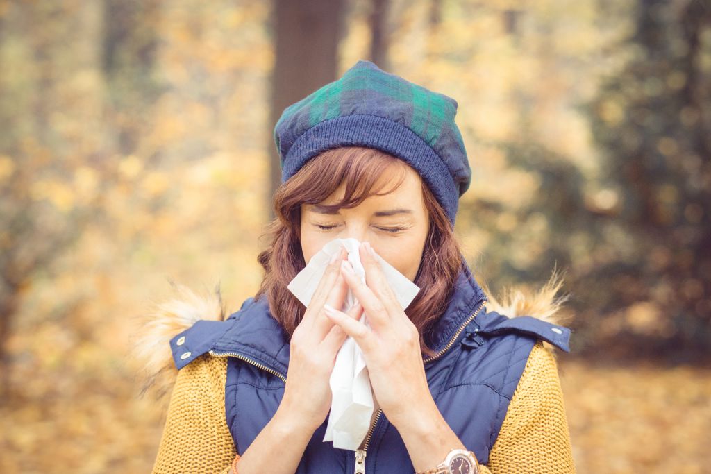 Junge Frau mit Atemwegsinfekt hält Taschentuch vor Nase